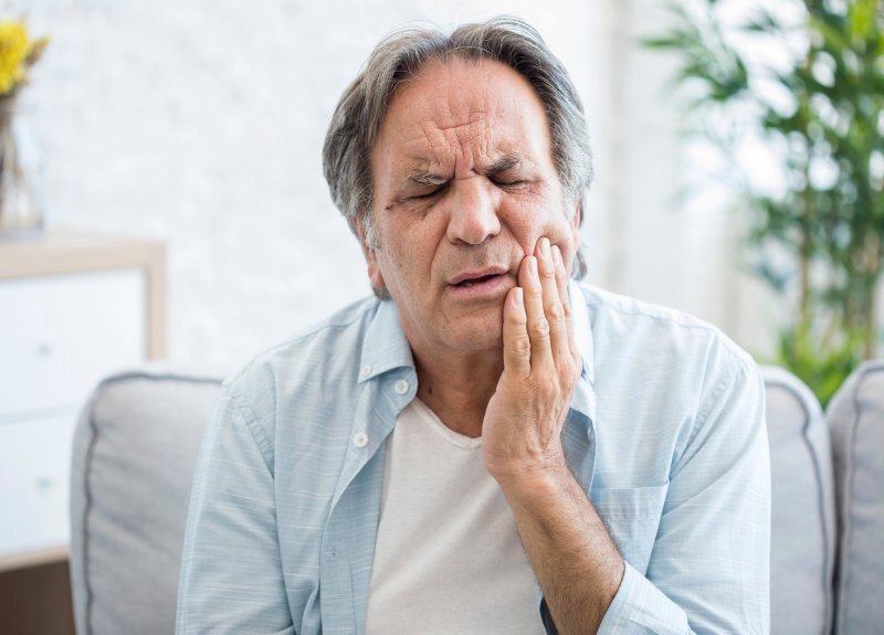 Middle-aged man holding his cheek in pain, illustrating jaw discomfort and dental problems.