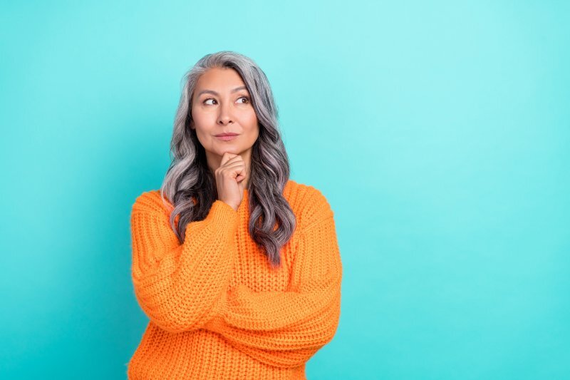 Woman in orange sweater considering dental implant options against turquoise background.