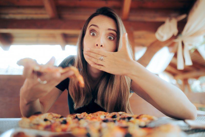 Woman covering her mouth in surprise while looking at pizza, illustrating taste problems.