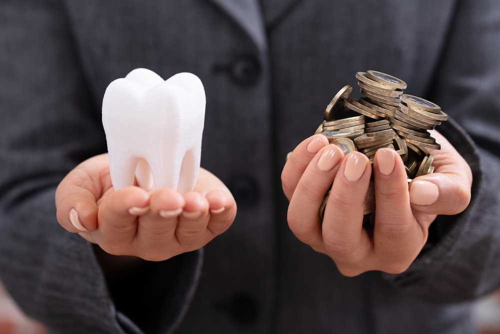 Young Woman's Hand Holding White Tooth And Coins Over Desk