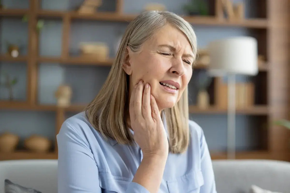 Woman holding her cheek in pain, showing signs of dental discomfort or toothache.
