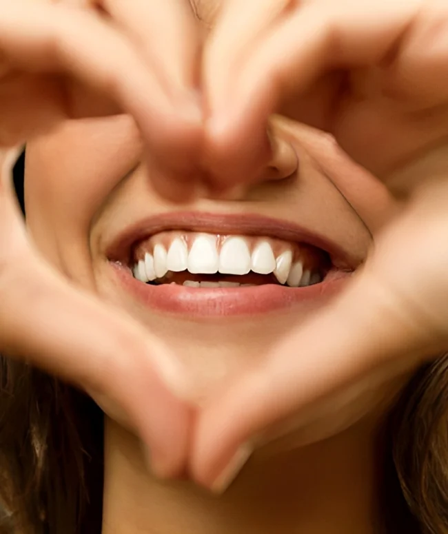 Close-up of a woman’s smile framed by her hands held in a heart shape