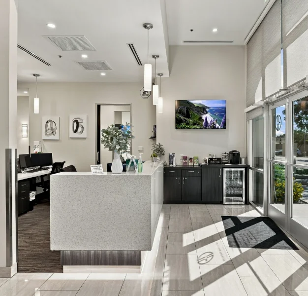 Modern dental office interior with glass partitions, treatment areas, and wall mounted televisions.