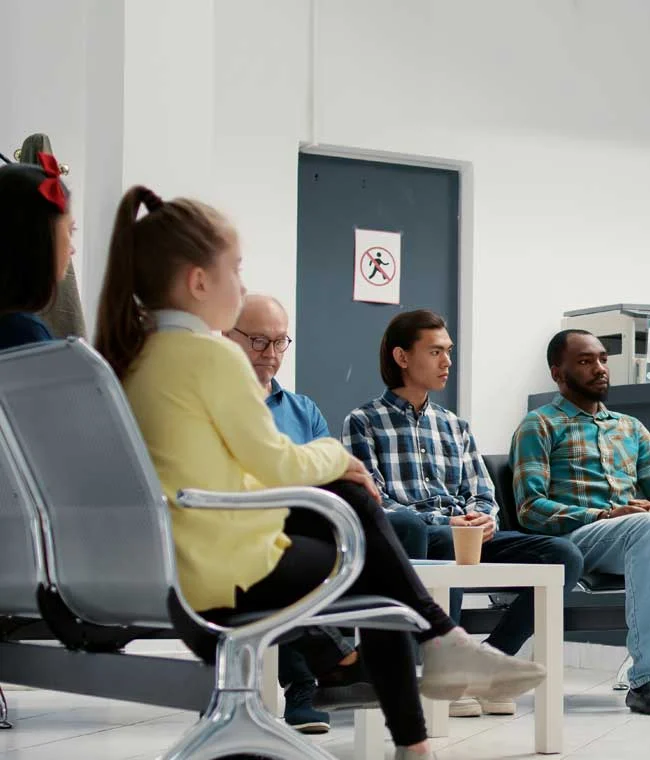 Patients of various ages seated in a dental office waiting room, with a coffee cup on a small table between them