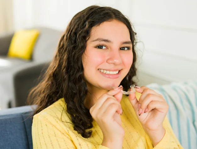 Teen girl holding a clear Invisalign aligner near her smile